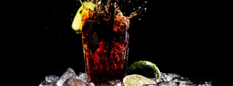 Fresh cola drink with splashes of water and green lime on black background
